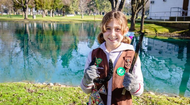 A young girl in a Girl Scout vest holds debris she found while magnet fishing.