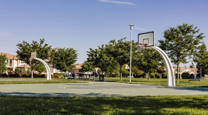 An image from a distance of 2 half basket ball courts with clear skies and  trees in the background