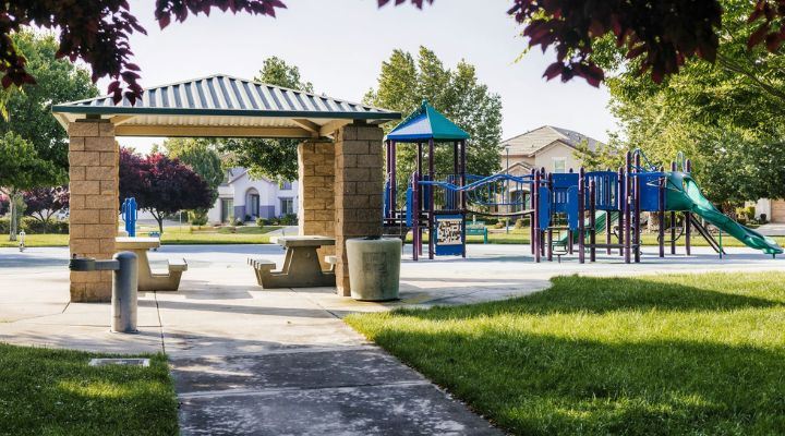 A tan brick shade structure with two picnic benches and a playground in the background