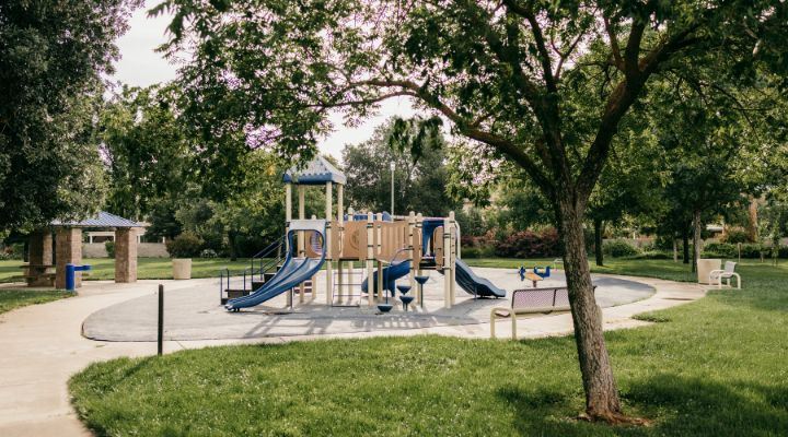 Image of a cream and blue playground with 2 park benches and a tree in the foreground