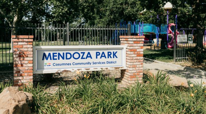 Sign that says "Mendoza Park" with flowering plants in the foreground in front of a park
