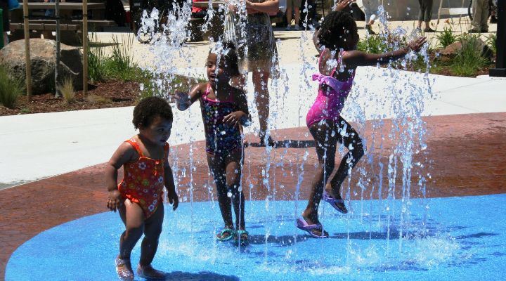 3 preschool-aged children splashing in a water feature