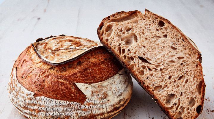 2 loafs of round sourdough bread, one is sliced in half and resting on the full loaf.