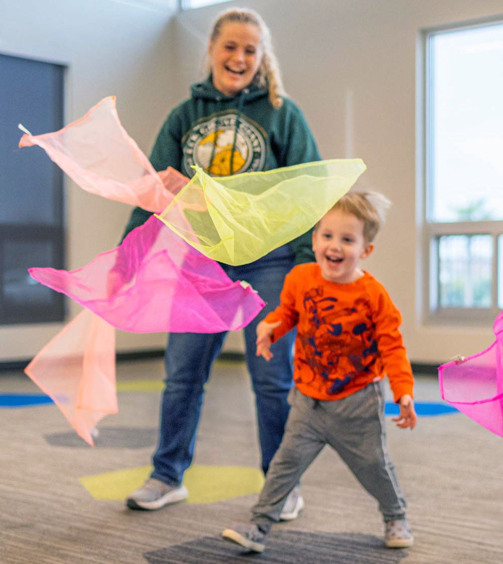 A teacheer plays with a student. Colorful translucent scarves fall around them.