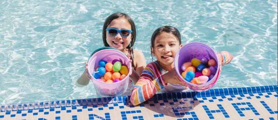 Two participants swimming in the pool showing off their Easter eggs. 